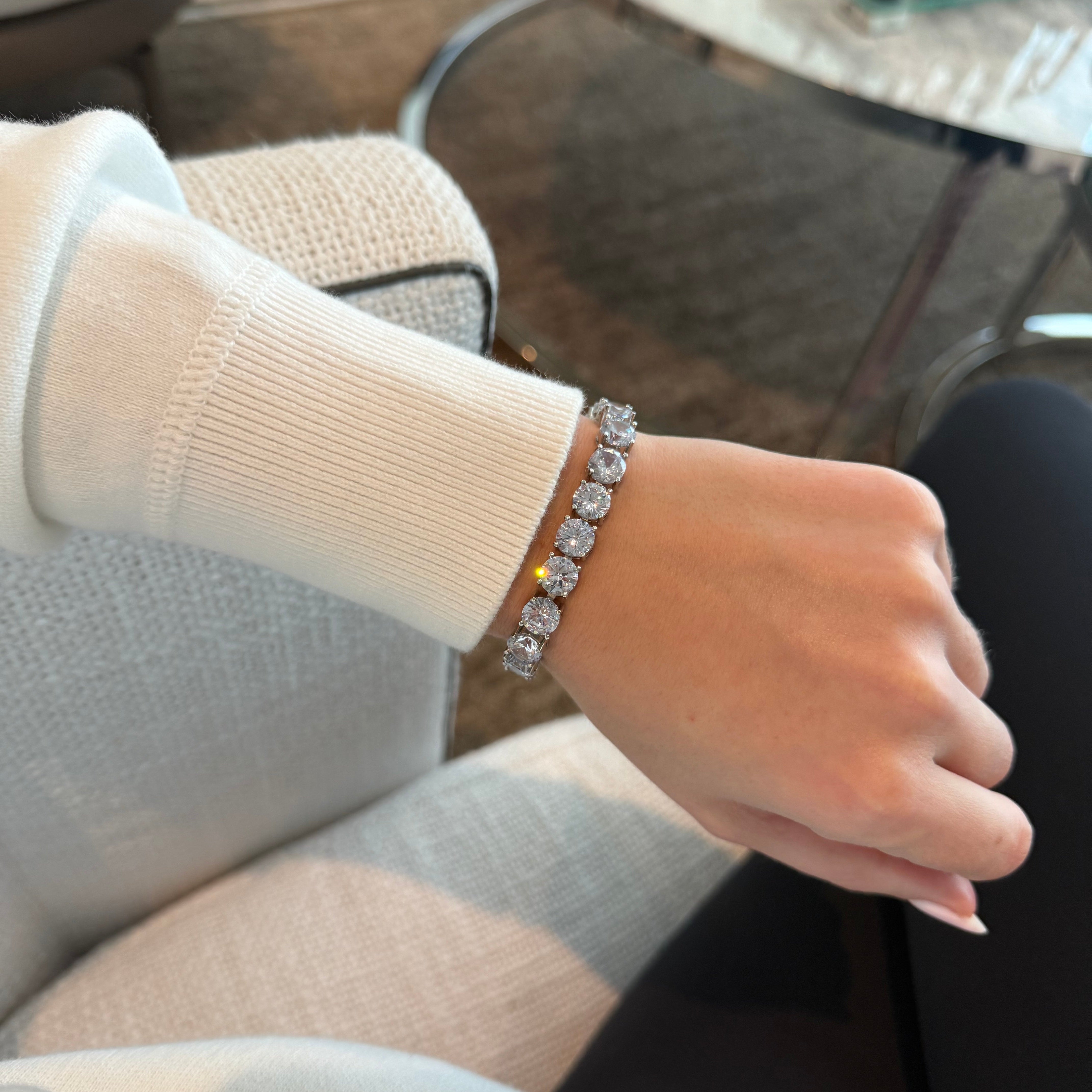 Hand wearing a diamond bracelet with a blurred indoor background