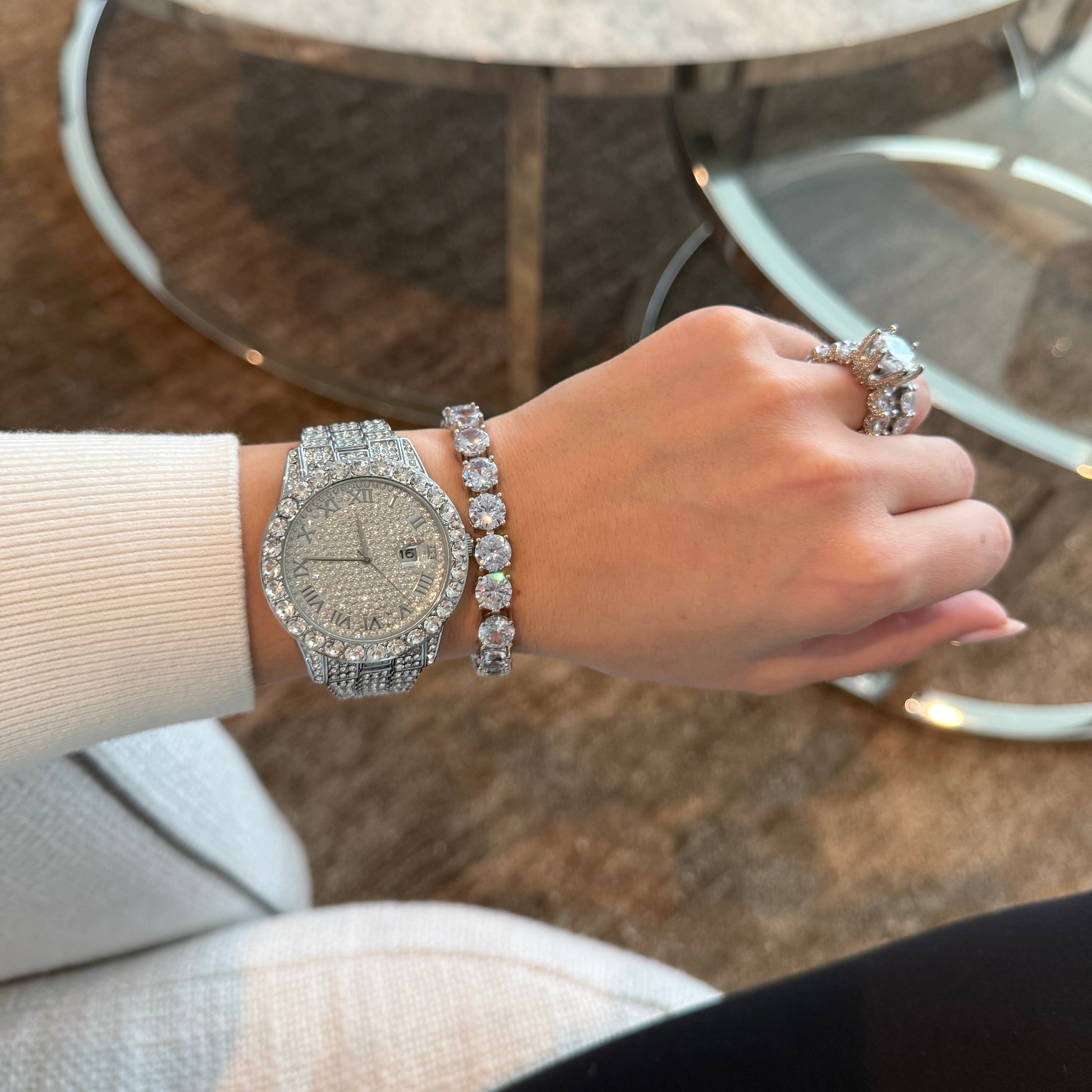 Hand wearing a silver watch and bracelet with a ring, blurred background