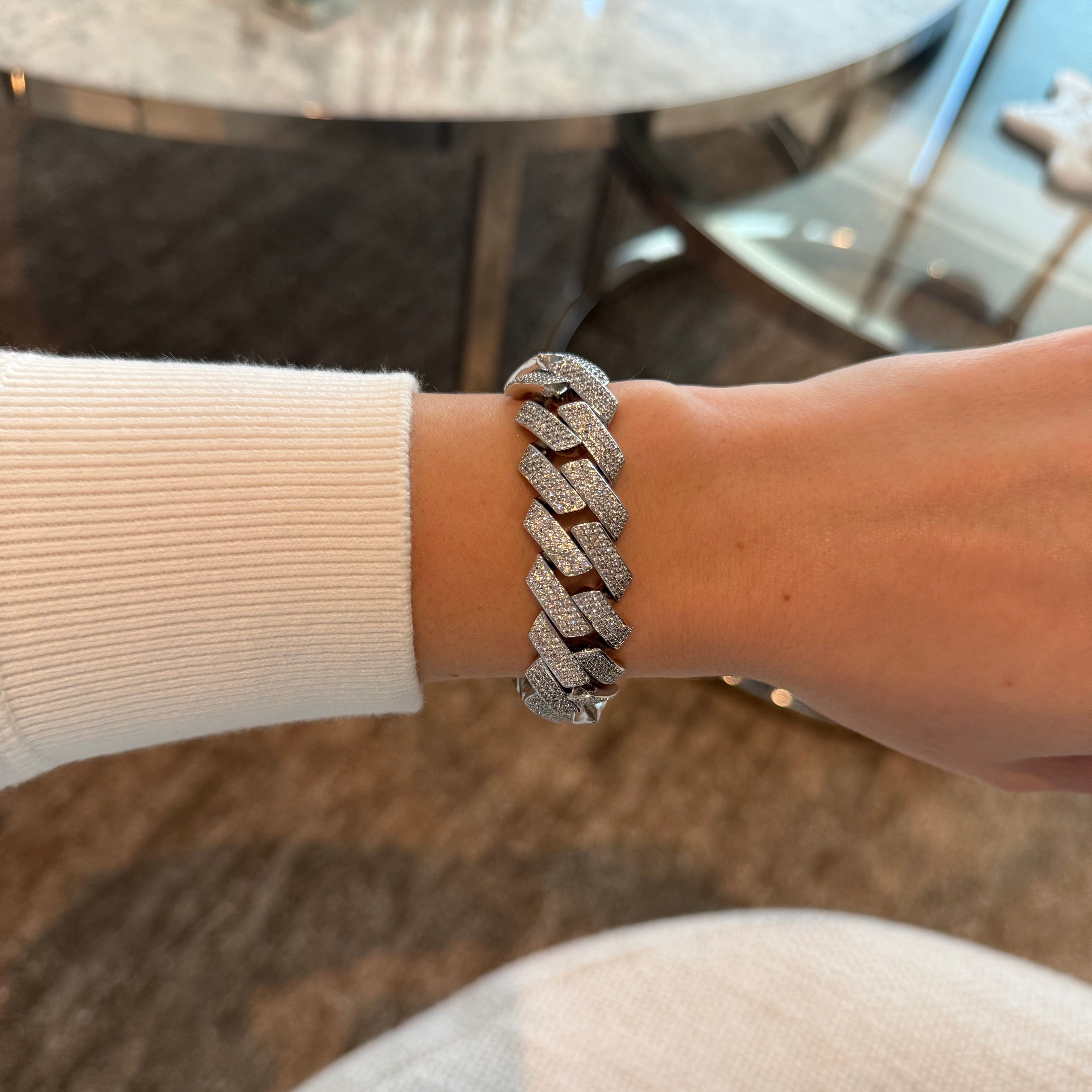 Close-up of a person's wrist wearing a silver chain bracelet with a blurred background.