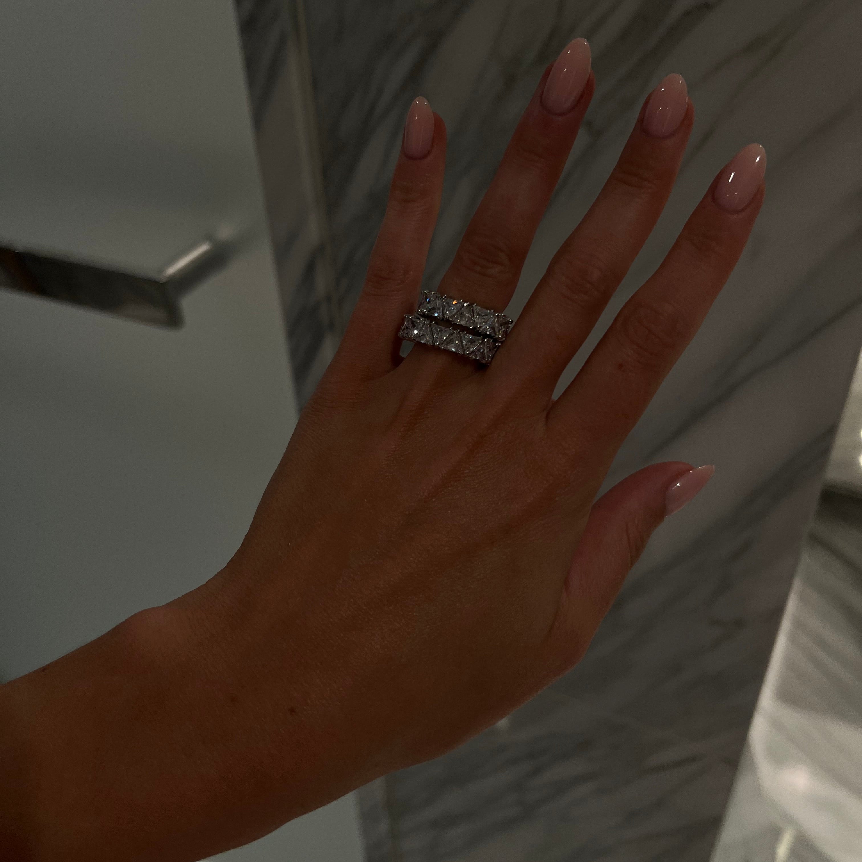 Hand wearing a diamond ring with a neutral background
