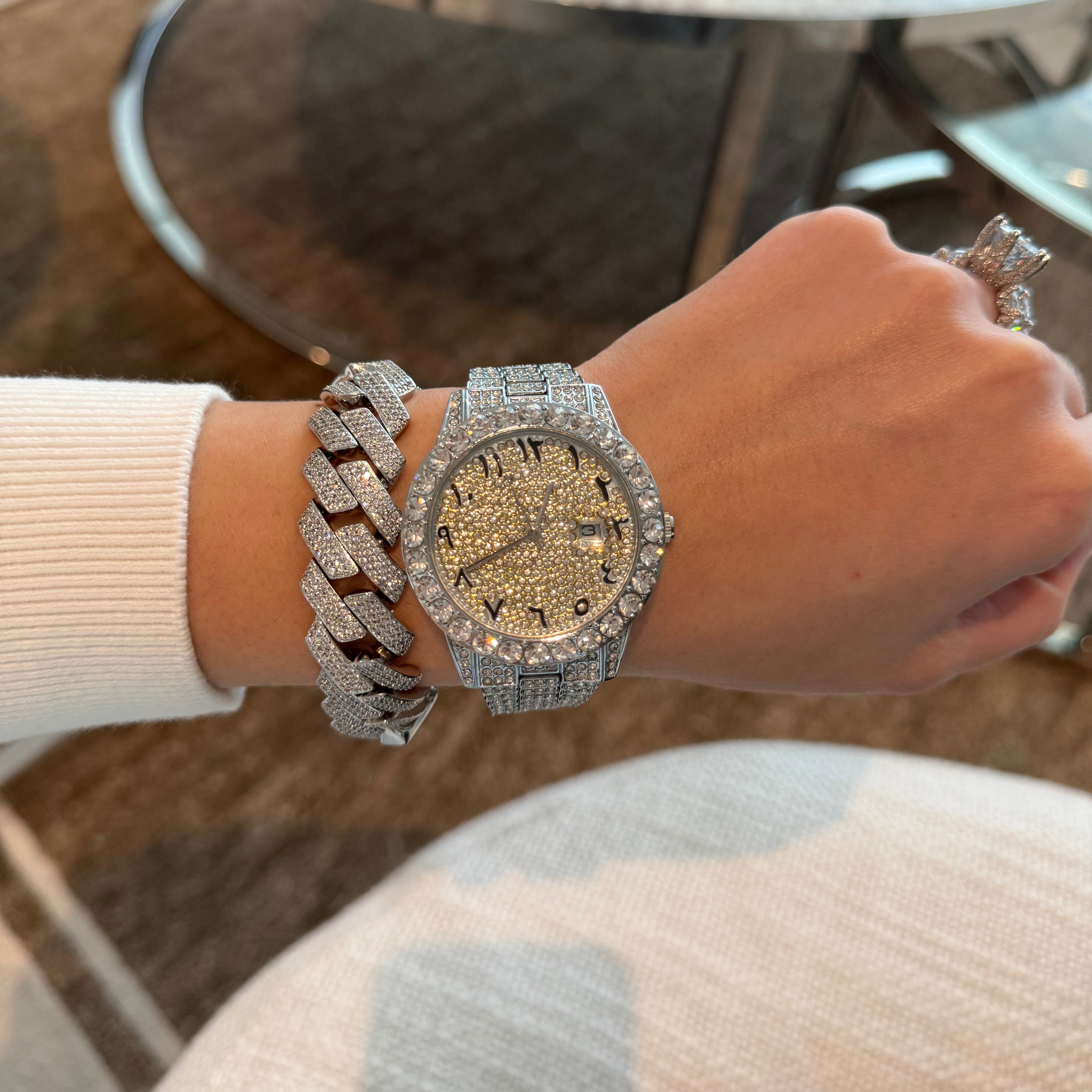 Hand wearing a silver watch with diamond accents and a silver chain bracelet, blurred background