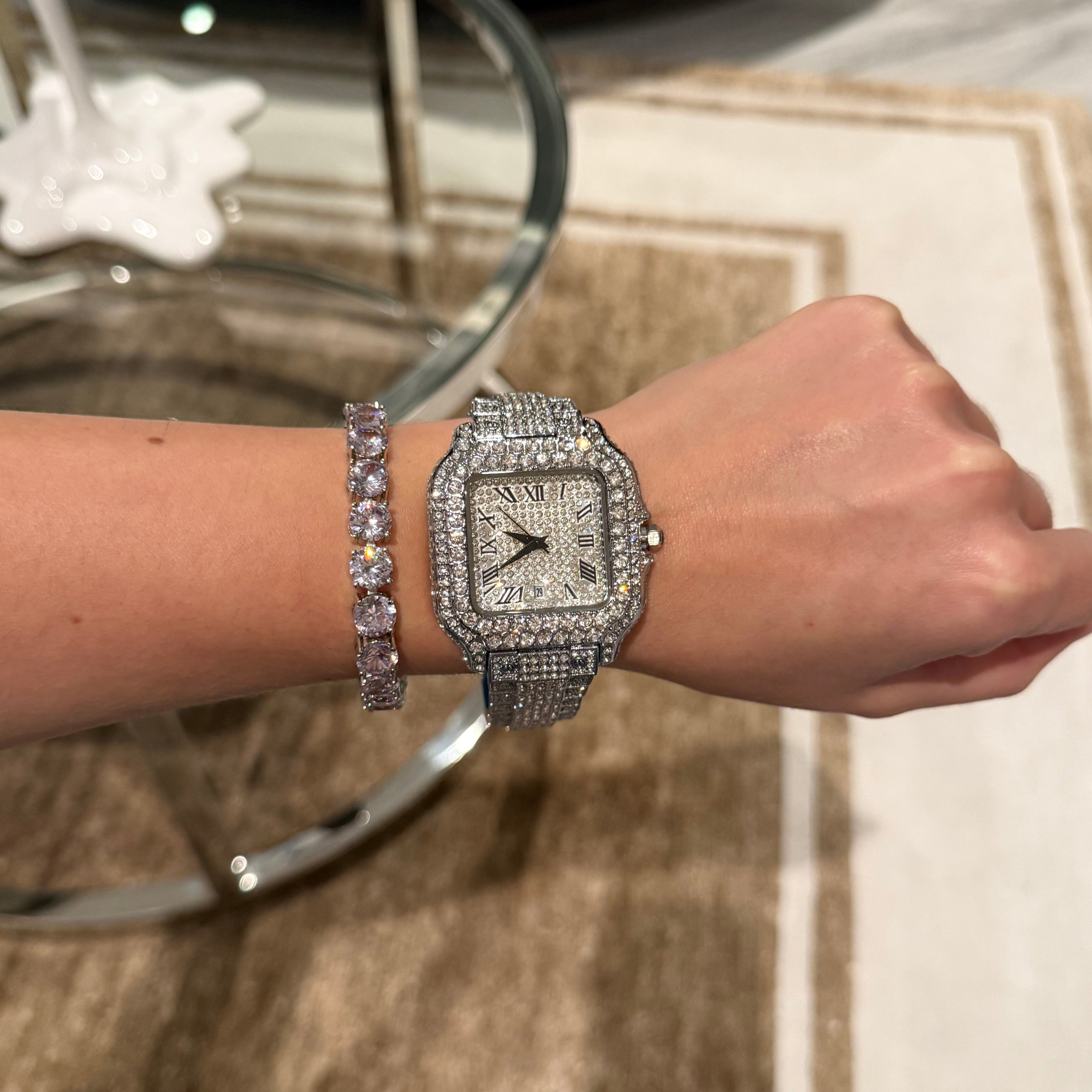 Silver watch with diamond accents on a wrist, with a matching bracelet, against a neutral background.